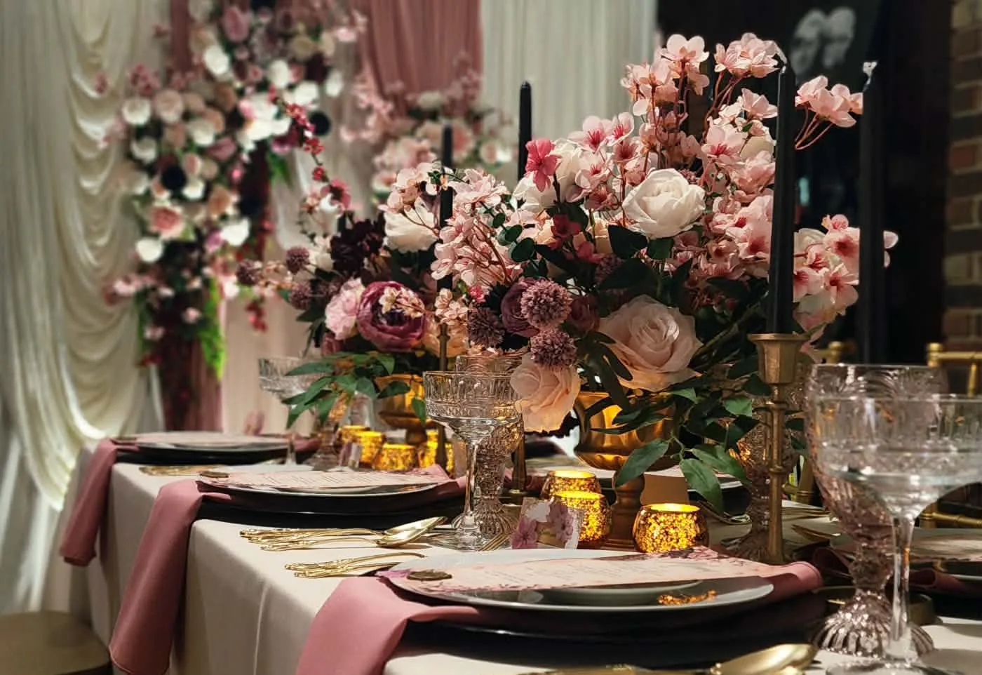 Romantic garden party table with cherry blossom centerpieces, black taper candles, and a floral draped backdrop